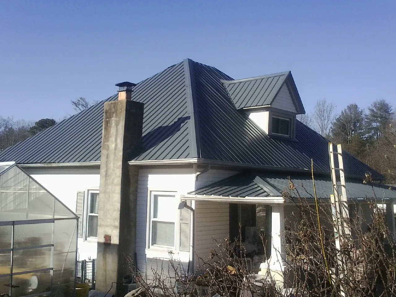 Dark blue standing seam metal roof on a white farmhouse with dormer — Slate & Tile Roof Repair by Roofing Brothers in Calhoun